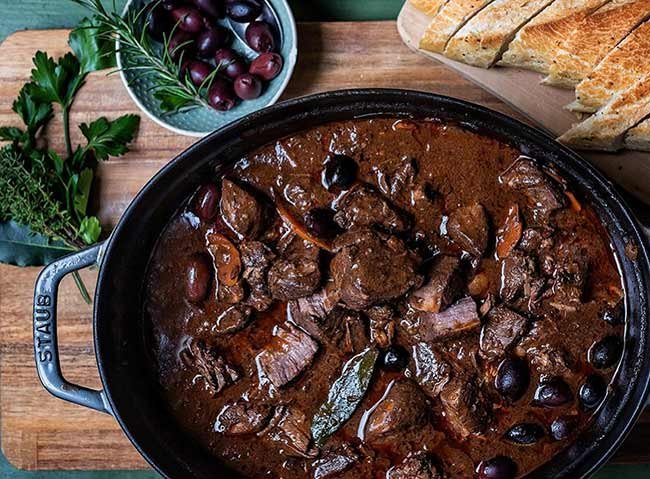 Ragoût de boeuf mijoté dans une cocotte noire, olives et morceaux de viande, accompagné de pain.